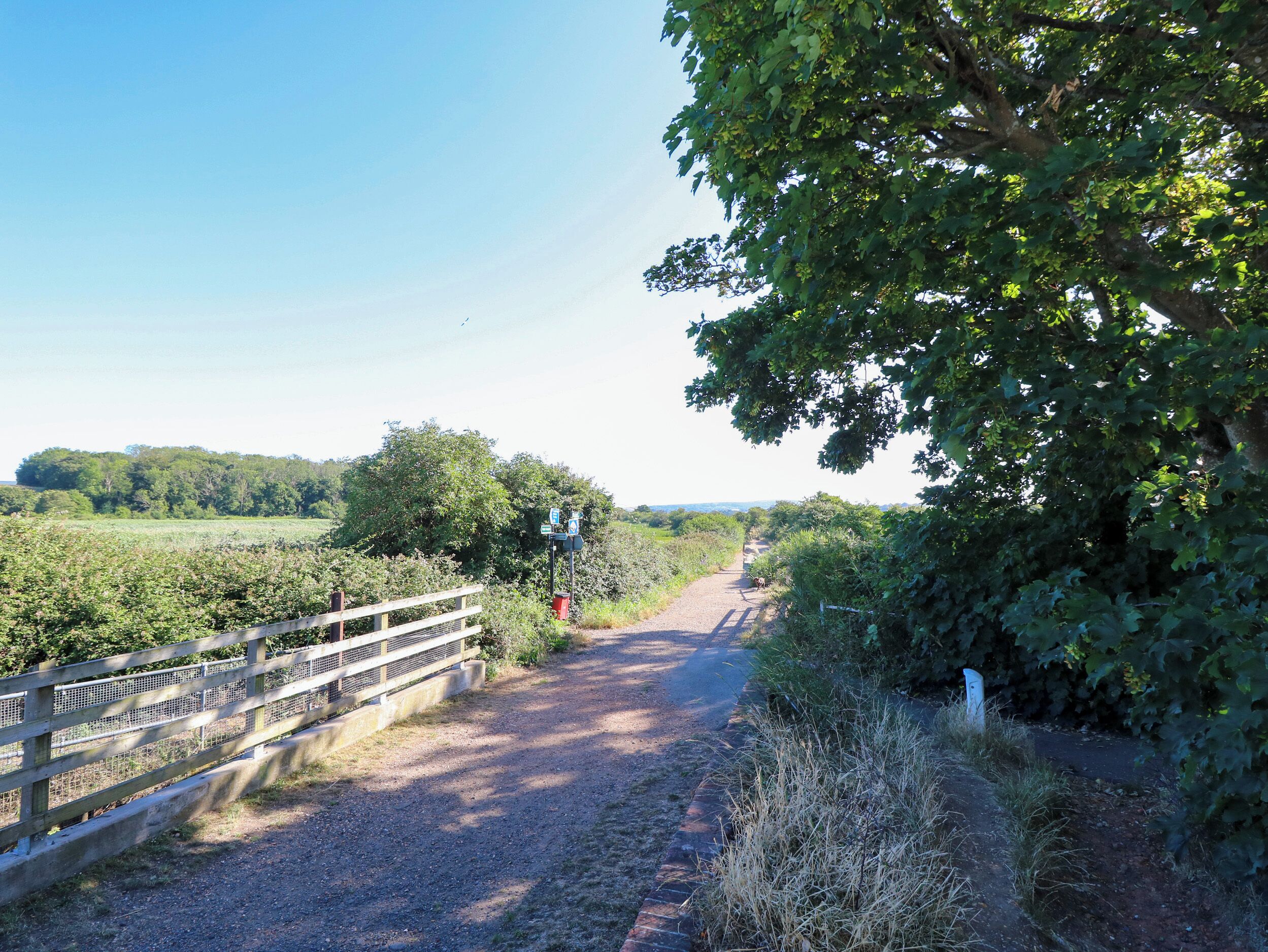 Un sentier rural bordé d’une clôture en bois et agrémenté d’un panneau indicateur.