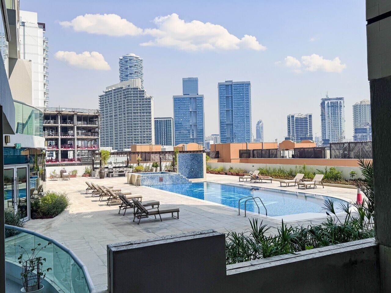 Una piscina en la azotea con sillas de descanso, vista del horizonte de una ciudad y edificios modernos al fondo.