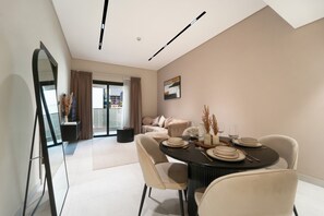 Un espace repas moderne avec une table ronde dressée pour quatre personnes, un canapé en arrière-plan et un grand miroir sur le côté gauche.