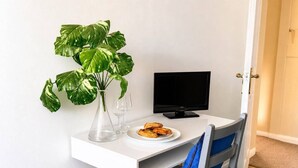 A small, white desk with a computer monitor, a clear vase with a plant, two wine glasses, and a plate of food. - Signature Room I (Egham station – 5 minutes walk) (Egham)
