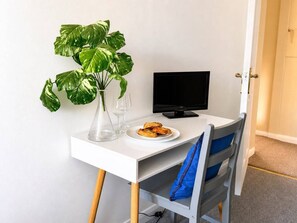 A small, white desk with a computer monitor, a clear vase with a plant, two wine glasses, and a plate of food. - Signature Room I (Egham station – 5 minutes walk) (Egham)