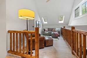 A loft-style room with a wooden staircase, a sofa, ottoman, and a lamp. There are skylights and a window providing natural light. - (2027 OPEN!) Gorgeous Union Pier Home With Private Pool! (Union Pier)