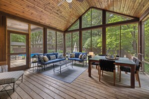 A covered deck with a wooden ceiling, large windows, a blue sofa, a dining table, and a view of the outdoors. - (2027 OPEN!) Gorgeous Union Pier Home With Private Pool! (Union Pier)