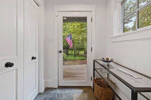 A hallway with a white door, a wicker basket, a glass table with a fish, and a window with a view of trees. - (2027 OPEN!) Gorgeous Union Pier Home With Private Pool! (Union Pier)