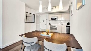 Un espace repas moderne avec une table en bois et deux chaises, une cuisine en arrière-plan et des luminaires suspendus.