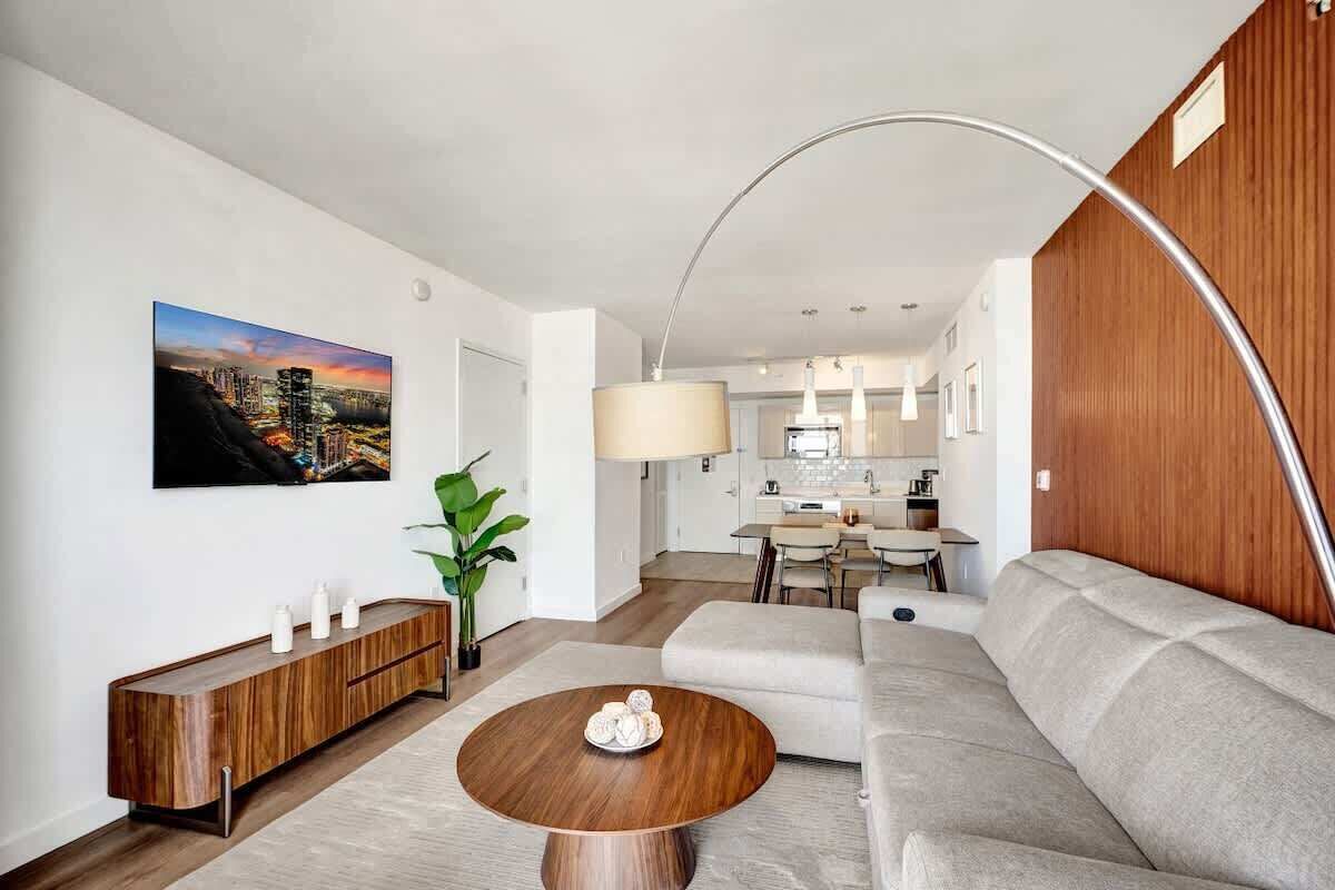 Un salon moderne avec un canapé, une table basse, une console en bois et un tableau représentant un paysage urbain.