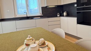 Moderni keittiö, jossa on valkoiset kaapit, musta työtaso ja ruokapöytä, jonka päällä on kudottu alusta.