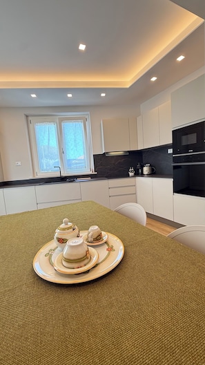 Una cocina moderna con armarios blancos, encimera negra y una mesa de comedor con un protector de mesa tejido.