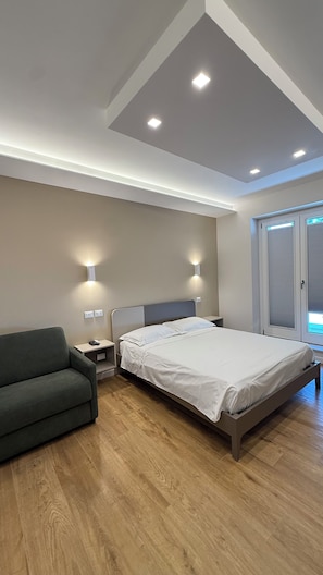 Un dormitorio moderno con cama, mesitas de noche, un sofá y una ventana con persianas.