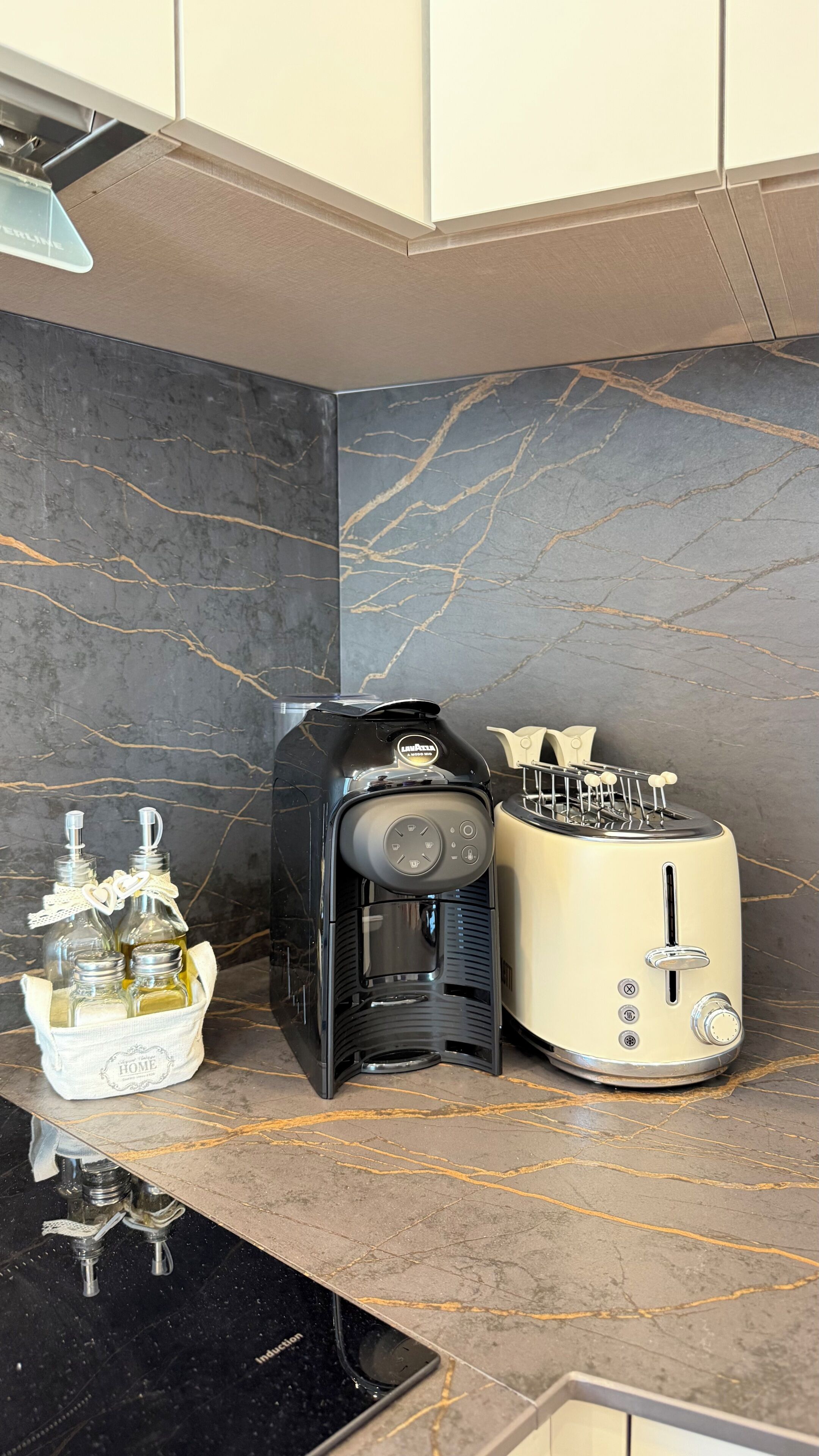 Una cocina con encimera de mármol, cafetera, tostadora y un portal botellas con botellas.