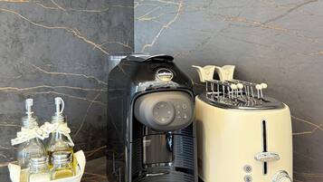 Una cocina con encimera de mármol, cafetera, tostadora y un portal botellas con botellas.