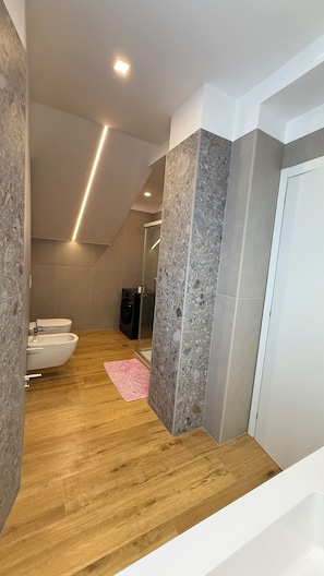 Un baño moderno con suelo de madera, una bañera blanca, un inodoro blanco y un bidé.