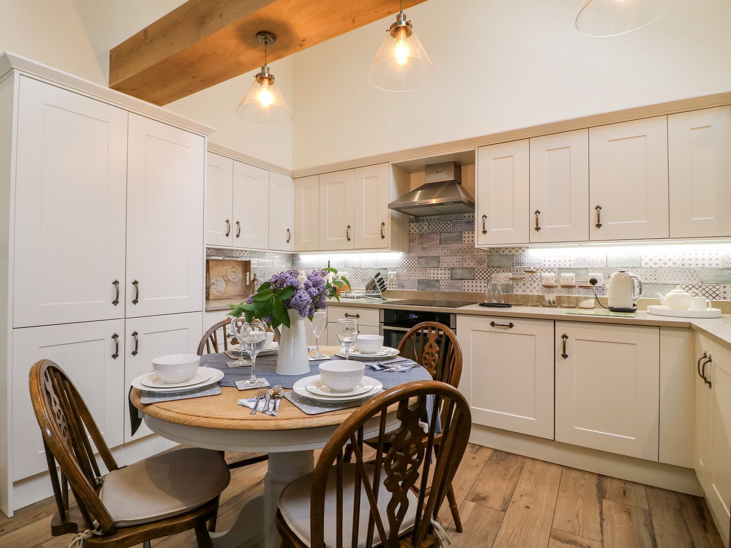 A kitchen with white cabinets, a wooden ceiling, and a dining table set for four.