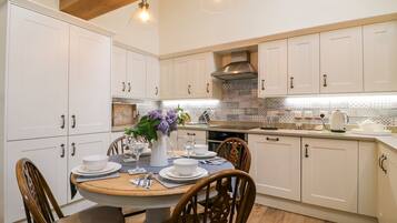 A kitchen with white cabinets, a wooden ceiling, and a dining table set for four.