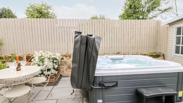 A hot tub with a cover, a table with chairs, and a bottle of champagne.