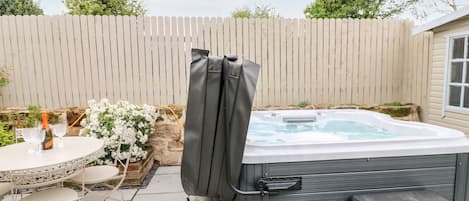 A hot tub with a cover, a table with chairs, and a bottle of champagne.