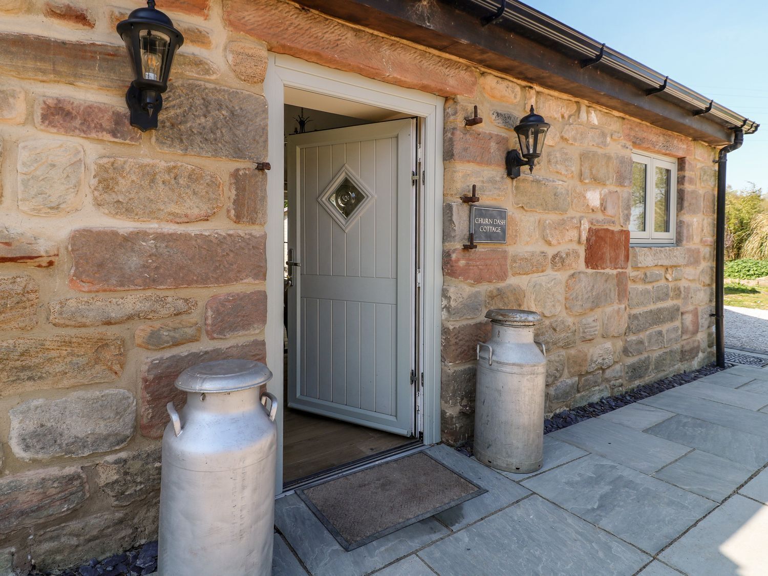 A stone cottage with a white door, two metal lanterns, and a sign reading 'CHURN DASH COTTAGE.'