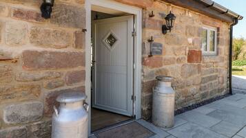 A stone cottage with a white door, two metal lanterns, and a sign reading 'CHURN DASH COTTAGE.'