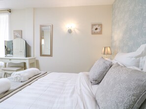 A hotel room with a bed, a bedside table with a lamp, a mirror, and a wall-mounted light fixture. - Churn Dash Cottage (Derby)