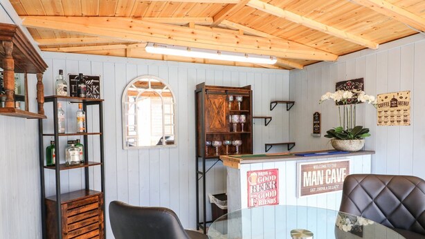 A bar area with wooden shelves, a glass table, and black leather chairs. - Churn Dash Cottage (Derby)