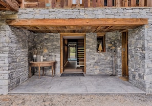 Ein Steinhaus mit einer Holzveranda, einer Treppe, die zu einer oberen Ebene führt, und einem Tisch mit Vasen.