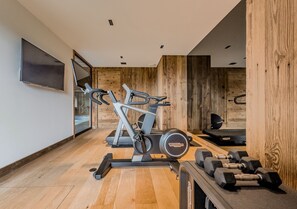 Ein Fitnessraum mit Trainingsgeräten, einem Fernseher und Holzwänden.