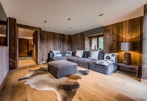 Ein modernes Interieur eines Blockhauses mit einer Eckcouch, einem Fellteppich und einer Lampe.