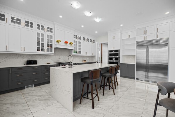 A modern kitchen with white cabinetry, a marble countertop, and stainless steel appliances.