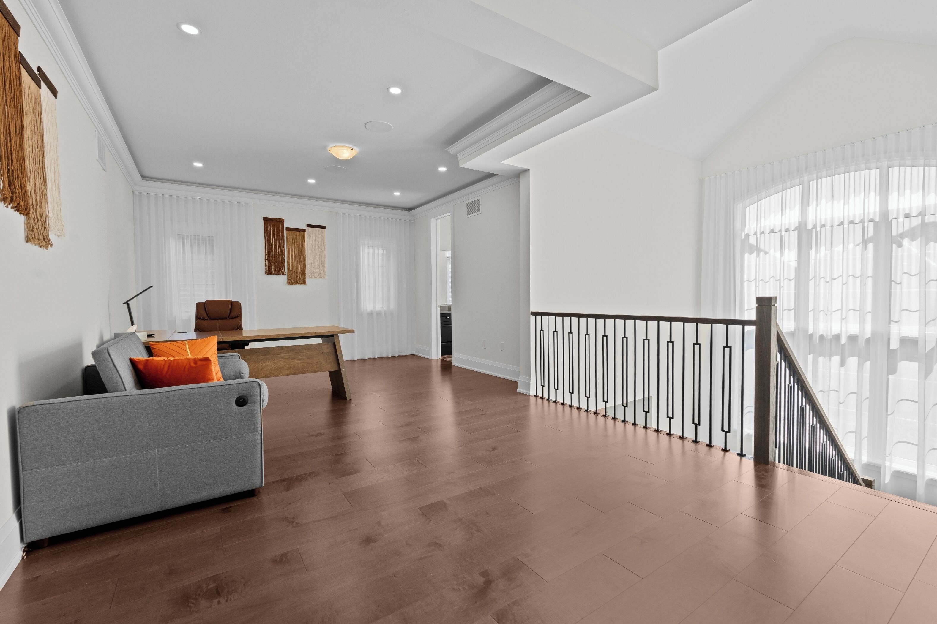 A spacious living area with a wooden floor, a grey sofa, a wooden coffee table, and a staircase with a railing.