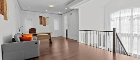 A spacious living area with a wooden floor, a grey sofa, a wooden coffee table, and a staircase with a railing.