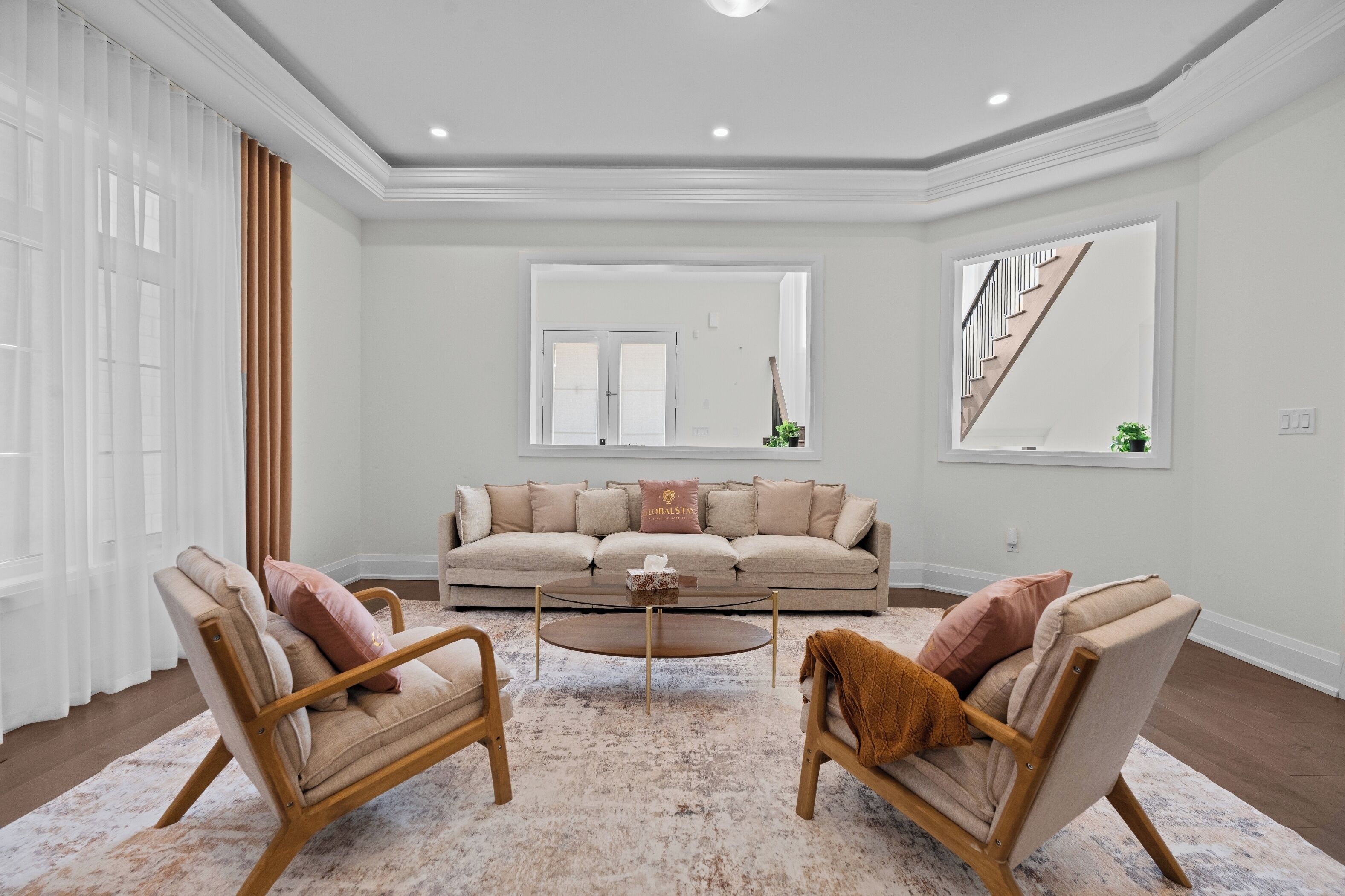 A spacious living room with a large sofa, two armchairs, a coffee table, and a view of a staircase.