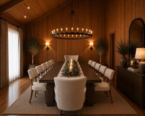 Ein Esszimmer mit einem langen Tisch, Stühlen, einer Chandelüstere, Wandleuchten und Topfpflanzen.