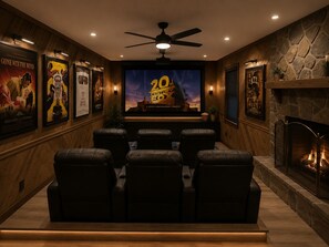 Ein Heimkino mit Ledersesseln, einem großen Bildschirm und einem Kamin.