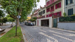 Une rue pavée bordée d’immeubles à plusieurs étages, de voitures garées et d’un banc.