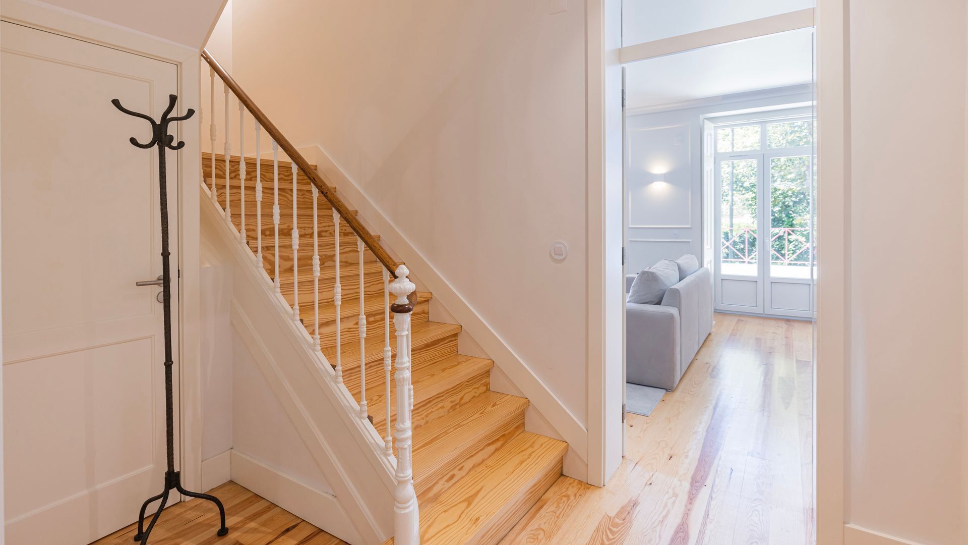 Un escalier avec des marches en bois et des balustrades blanches menant à une pièce où se trouve un canapé gris et une grande fenêtre.