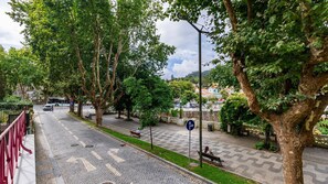 Calle adoquinada bordeada de árboles y bancos, con un autobús a lo lejos.