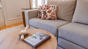 Ein modernes Wohnzimmer mit einem grauen Sofa, einem runden Couchtisch und einem Buch mit dem Titel 'CREATE AT HOME WITH OLD & NEW'.
