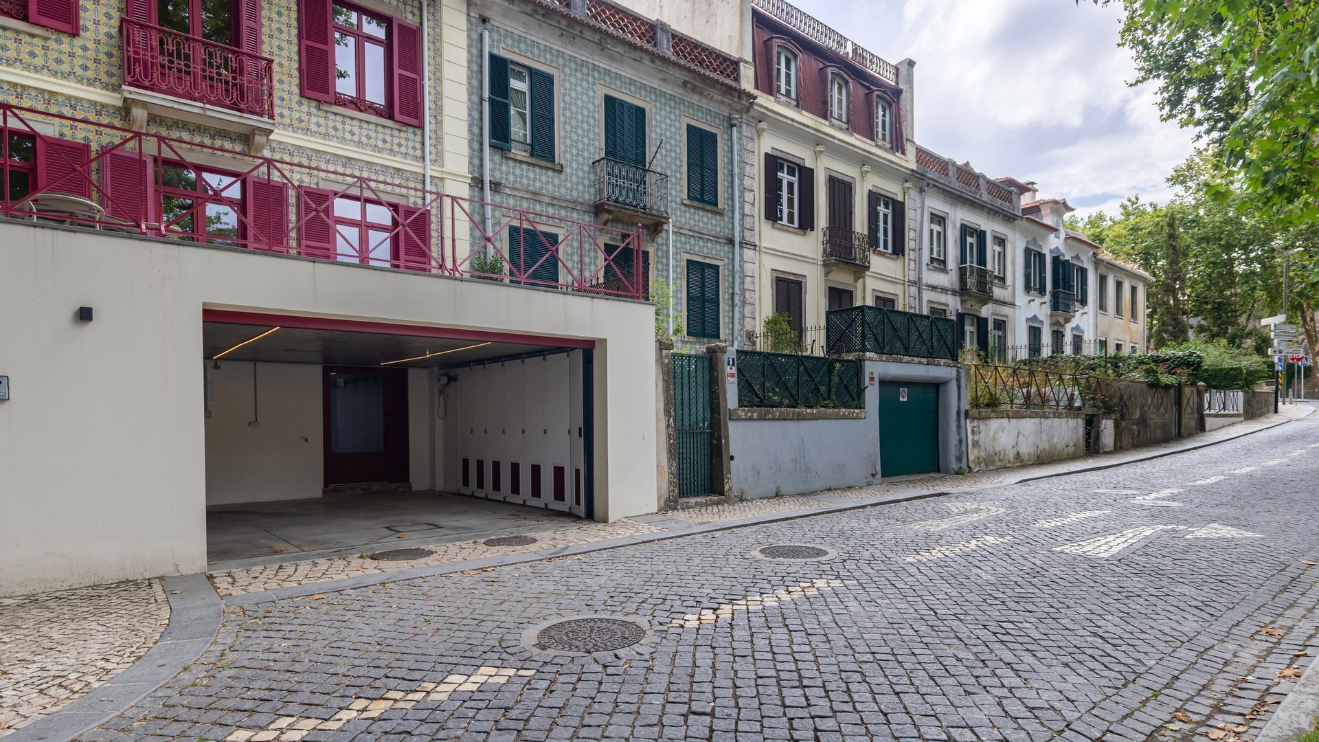 A cobblestone street with a row of buildings featuring balconies and a garage entrance.