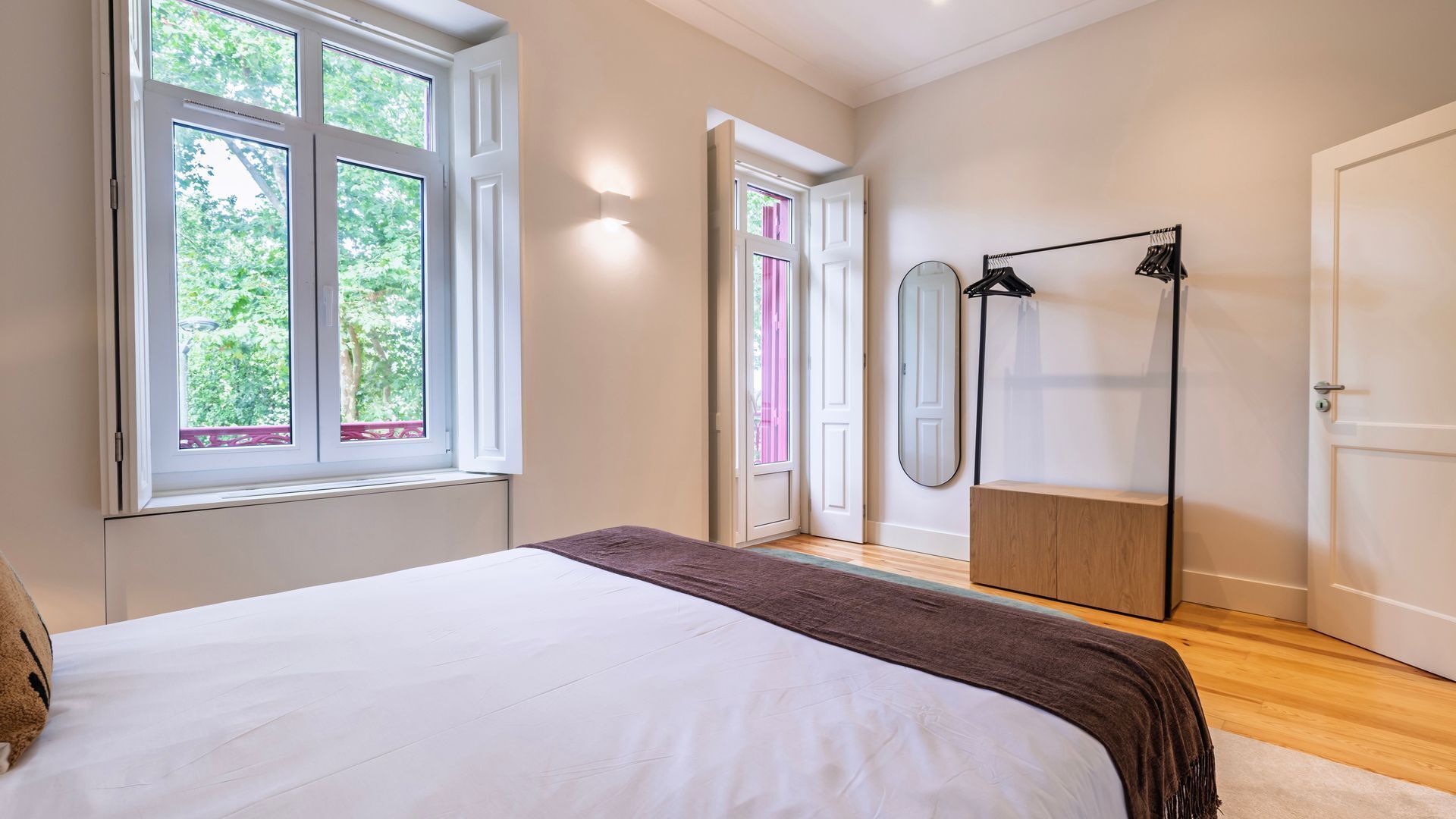 A bedroom with a large bed, a wardrobe, a mirror, and a door leading to another room.