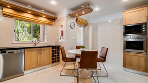 A modern kitchen with a dishwasher, oven, and dining area with chairs and a table. - Casa V2 Solarenga perto de Ferragudo by Lovelystay (Ferragudo)