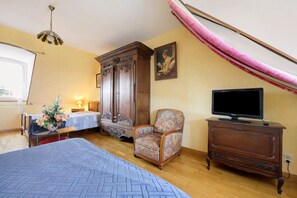 Ein Schlafzimmer mit einem Bett, einem Holzschrank, einem Sessel, einem Fernseher und einem Bild an der Wand.
