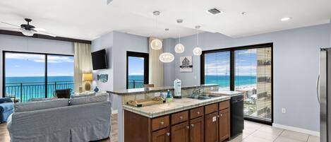 A modern kitchen with a large island, a dining area with a view, and a living room with a sofa.