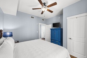 Ein Schlafzimmer mit Bett, Deckenventilator, Kommode, Fernseher und einer Tür.