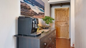 Una kitchenette con cafetera, una planta en maceta y una puerta de madera al fondo.