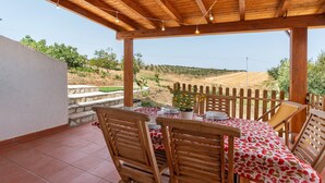 Un patio exterior con una pérgola de madera, una mesa lista para cenar y vistas a un viñedo.