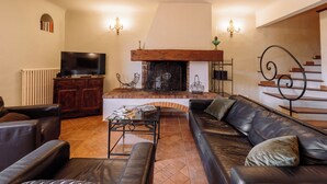 Una sala de estar con chimenea, sofás de cuero, televisor y escalera.