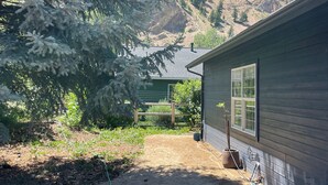 Ein Haus mit Schotterhof, einem großen Baum und einem Berg im Hintergrund.