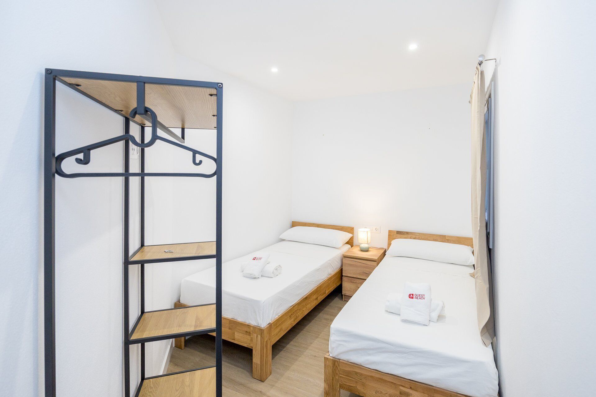 Een kleine, schone kamer met twee eenpersoonsbedden, een houten wandplank en een kledingrek.