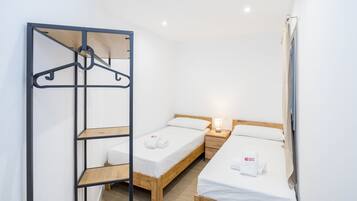 Een kleine, schone kamer met twee eenpersoonsbedden, een houten wandplank en een kledingrek.