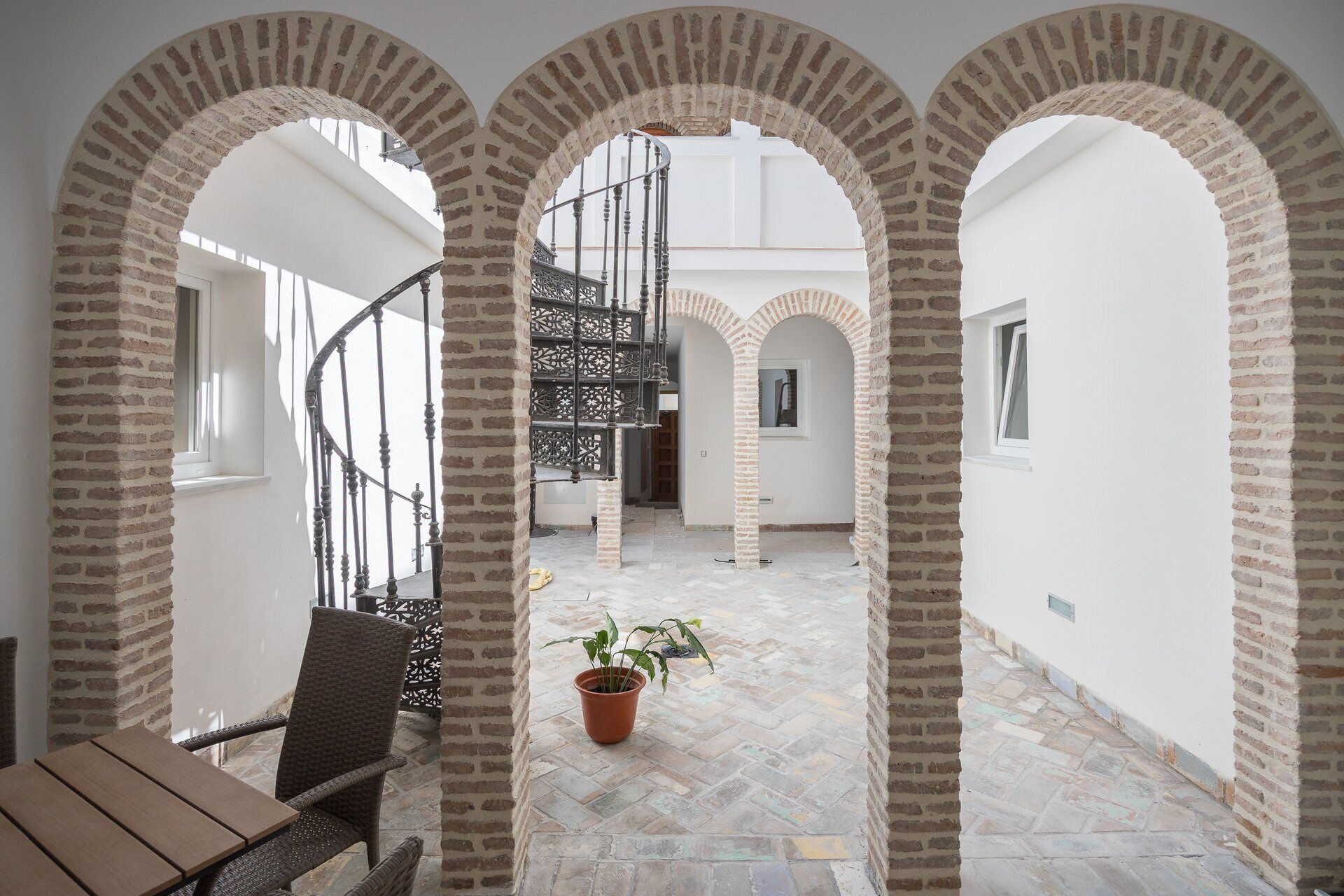 Un patio con arcos de ladrillo, una escalera en espiral y una planta en maceta.